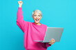 © Pixels Hunter - Woman celebrating success holding laptop against bright blue background.