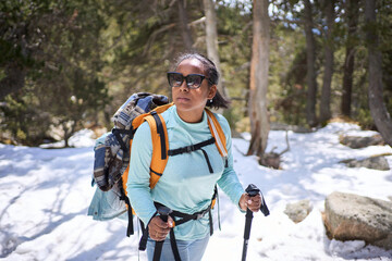 female hiker enjoying a snowy mountain forest trail, equipped with backpack and trekking poles, embr