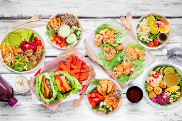 Wall Mural - Healthy take out fast food table scene. Top view over a white wood background. Lettuce bean burgers with sweet potato fries, nutritious bowls, lettuce wraps and smoothie drink.