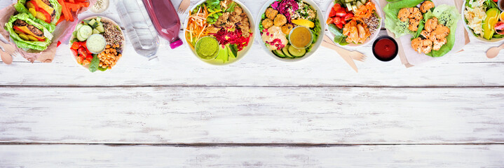 Wall Mural - Healthy take out fast food top border. Overhead view over a white wood banner background. Table scene with lettuce bean burgers, nutritious bowls and lettuce wraps. Copy space.