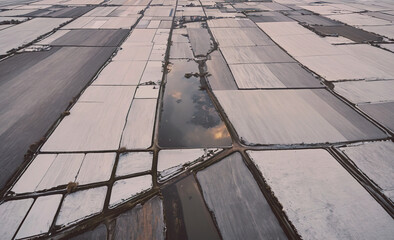 Poster - Large field of snow and ice with a few small patches of green. The sky is cloudy and the sun is setting