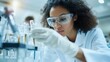© Jaroon - A woman in a lab coat is wearing safety goggles and gloves as she works with chemicals. She is focused on her task and she is in a serious mood