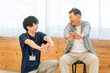 © buritora - リハビリで体操をする車椅子に乗ったシニア男性と理学療法士・作業療法士の男女スタッフ
