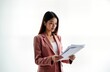 Asian businesswoman in pinkish-red suit examines important documents. Carefully studies financial papers. Focused, professional look. Successful businesswoman reviews business proposals. Setting in