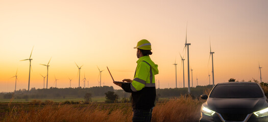 Aufkleber - Engineer working on laptop in front of wind turbines for checking wind turbines of the field during beautiful sunset. Alternative energy concept.