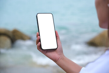 Wall Mural - mockup image of a woman holding mobile phone with blank desktop screen by the sea