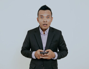 Wall Mural - Shocked asian businessman holding a mobile phone looking to camera, isolated over white background.