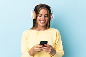 Young Uruguayan woman isolated on blue background listening music and looking to mobile