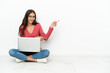 © luismolinero - Young French girl sitting on the floor with her laptop pointing finger to the side