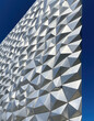 © Dolgren - Architectural Facades: Reflective Geometric Facade with Metallic Triangular Panels and Sharp Edges Under Clear Blue Sky