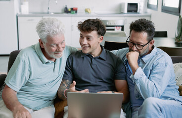 Sticker - Happy multigenerational family sitting on sofa using laptop together - grandfather with mature son and young grandson enjoying carefree moments together