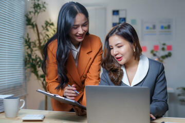 Wall Mural - Businesswomen working together analyzing financial data using laptop and clipboard in modern office