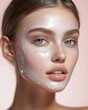 © irina - Close-up of a young woman applying a facial mask, showcasing clear skin and natural beauty against a soft pink background