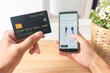 © Tito Rollis - Pov first person holding black mockup credit card for online shop on smartphone at home