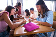 © CarlosBarquero - Female primary school teacher explaining in class to diverse group of students sitting at desks together. Young woman tutoring of elementary academy children gathered in the study hall. Back to school