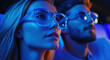 © Саша Федюк - A young woman and man are captivated by a performance in a colorful setting. Their unique glasses reflect the vibrant blue hues around them, enhancing their experience.