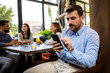 © Mediteraneo - Stressed businessman using his phone in the restaurant with his friends in the backround.