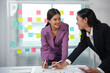 © amnaj - Two asian businesswomen discussing and working together on a project in an office with colorful sticky notes on a glass wall