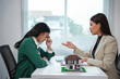 © amnaj - Real estate agent explaining contract terms to a stressed homebuyer with a miniature house model on the table