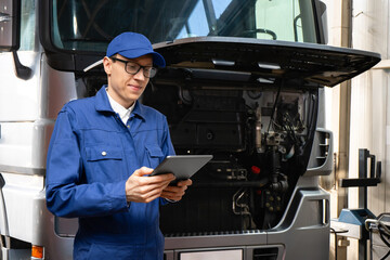 Poster - Serviceman with digital tablet on the background of the truck in the car service.