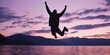© THINGDSGN - silhouette of a man jumping with joy by a serene lake during a purple and pink sunset, with mountains and clouds in the background creating a peaceful and inspiring atmosphere