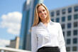 © Minerva Studio - Smiling businesswoman standing in front of office buildings in business district