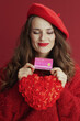 © Alliance - happy modern woman in red sweater and beret with red heart