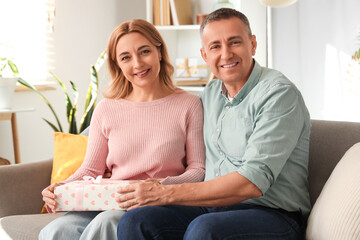 Wall Mural - Middle-aged couple with gift box sitting on sofa at home. International Women's Day