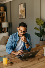 Wall Mural - Man seated at a table reviewing expenses while typing on his laptop