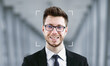 © Prostock-studio - A man in formal attire smiles while facial recognition software identifies him. The background features soft architectural lines, enhancing the focus on identification technology.