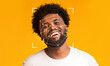 © Prostock-studio - A joyful man with curly hair smiles against a bright yellow backdrop. Overlayed are facial recognition markers, illustrating the use of identification technology in everyday life.