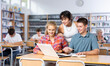 © JackF - Three fifteen-year-old schoolchildren, looking for information on a laptop and taking abstracts in a copybook, preparing for lessons in the school library