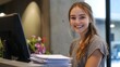 © Alex Piatkowski - A smiling young woman working at a modern reception desk, with a stack of neatly arranged documents.