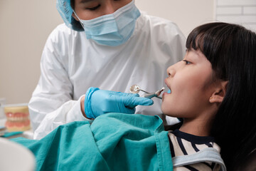 Wall Mural - Asian female pediatric dentist checks and examines a little Thai girl's caries teeth in dental clinic, well-being mouth oral hygiene, and professional orthodontic healthcare work in a kid hospital.