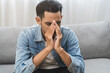 © KMPZZZ - Sad upset, frustrated alone asian young man headache thinking about finance problem, difficulty, feeling failure and exhausted, suffering from loneliness sitting on couch at home. Grief sorrow, bad.