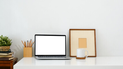 Wall Mural - Minimalist workspace featuring a laptop with a blank screen, mug, picture frame, and a pencil holder