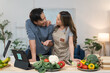 © crizzystudio - Young smiling asian couple cooking healthy meals together in a modern kitchen, following a recipe on a tablet, enjoying conversation and sharing laughter while preparing fresh ingredients