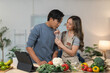 © crizzystudio - Young asian couple having fun preparing healthy meal together in modern kitchen, woman holding a glass of water for her husband, following online recipe on digital tablet