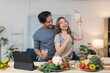 © crizzystudio - Young asian couple cooking together recording live video with tablet in kitchen, woman raising glass celebrating successful online sales and man hugging her