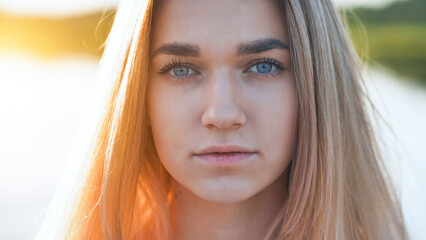 Portrait of a blonde teenage girl with blue eyes and a serious expression, enjoying the golden hour light in a natural outdoor setting