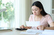 © Antonioguillem - Perplexed asian woman checking receipt at home