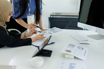 Wall Mural - Young businesswoman adviser standing in front of laptop and giving advise to sales woman. Business people consulting at office. asian teamwork concept.
