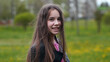 © Довидович Михаил - Teenage girl with long brown hair smiling, wearing leather jacket, standing in lush green park during sunny spring afternoon