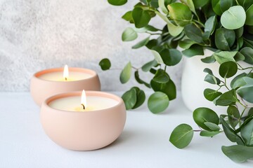 Aufkleber - Two pink candles with burning wicks and green plant on a white surface against gray background