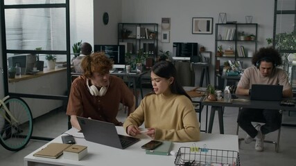 Two Caucasian young software developers discussing solution to tech problem during workday in modern office