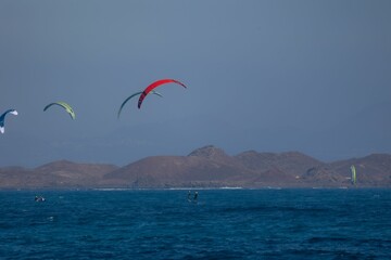 Kitesurfers with vibrant kites and mountain backdrop.