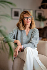 Poster - Beautiful woman sitting in an amrchair in her cozy home and smiling at camera