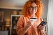 © Miljan Živković - smile redhead woman use mobile phone and credit card for payment