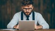 © Sirichai - Focused Professional: A bearded man with stylish glasses intently works on his laptop, showcasing dedication and concentration in a professional setting.