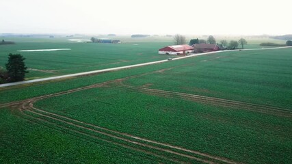 Wall Mural - cars going on a long rural road in vast green fields with rural houses and barns under misty sky